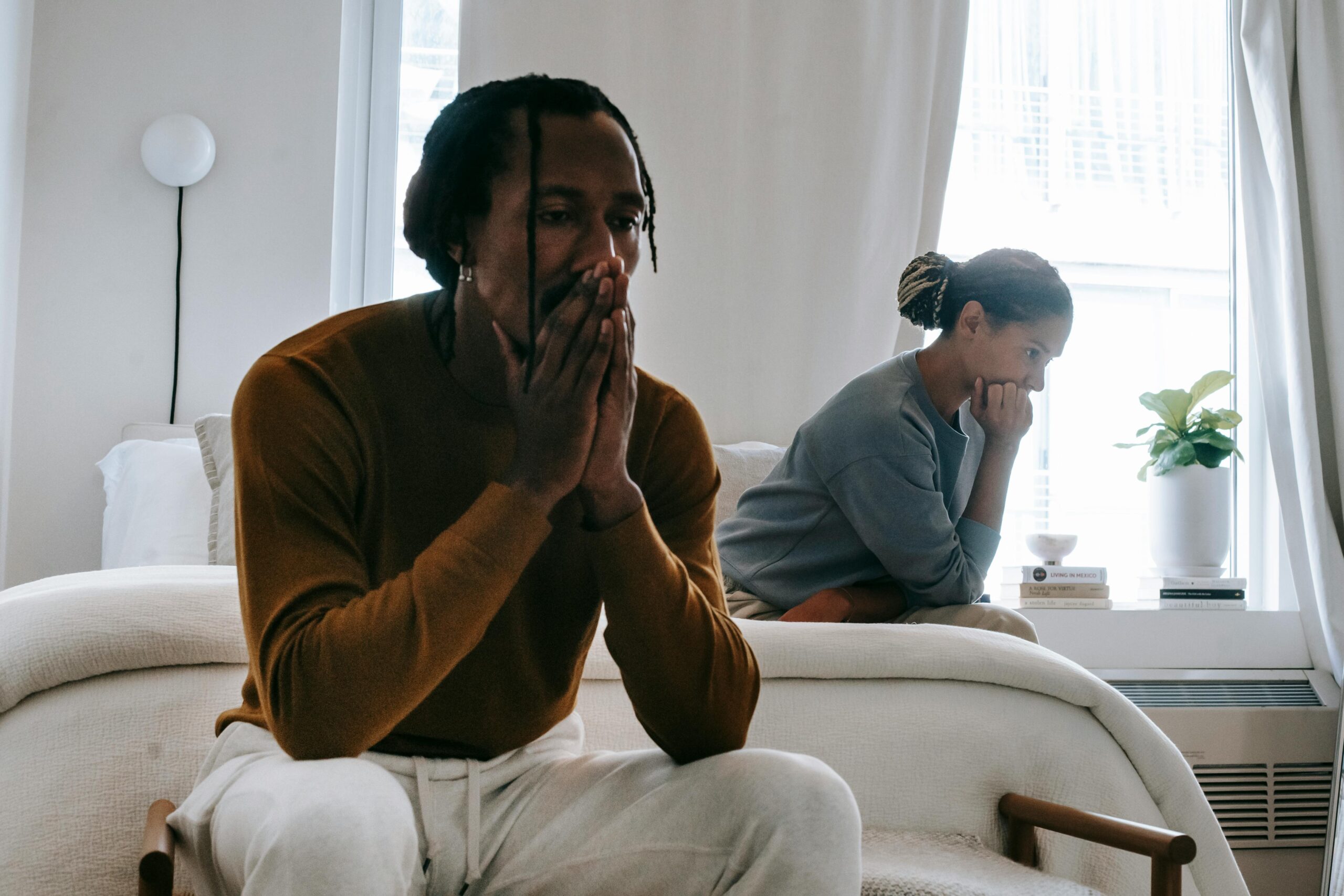A couple sitting at opposite sides of a room with their heads in their hands.